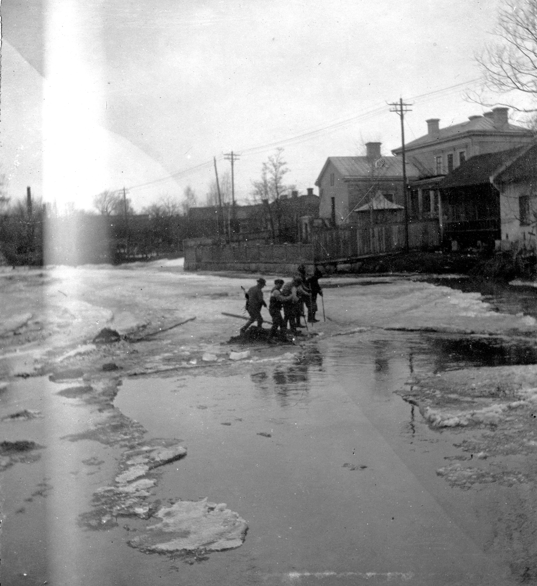 Fem män på ett isflak, ett bostadshus i bakgrunden. Fotograf Alfred Bergendahl. Givare H Bergendahl.