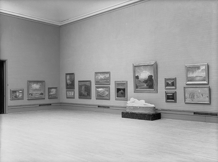 Prins Eugens utställning.
På väggen hänger flera tavlor och framför dem syns en liggande
vit skulptur.