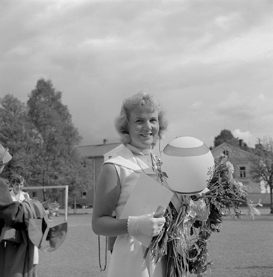 Sjuornas avslutning, 11/6 1955. 
En ung kvinna har ställt upp sig för fotografering på skolgården 
till dåv. Växjö Högre Allmänna Läroverk. 
I bakgrunden skymtar några av byggnaderna till dåv. Växjö lasarett.