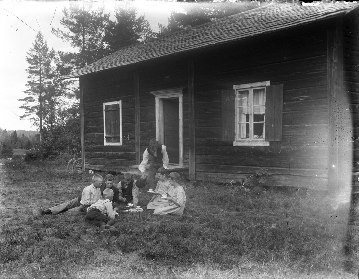 Barn dricker kaffe i gräset utanför hus.