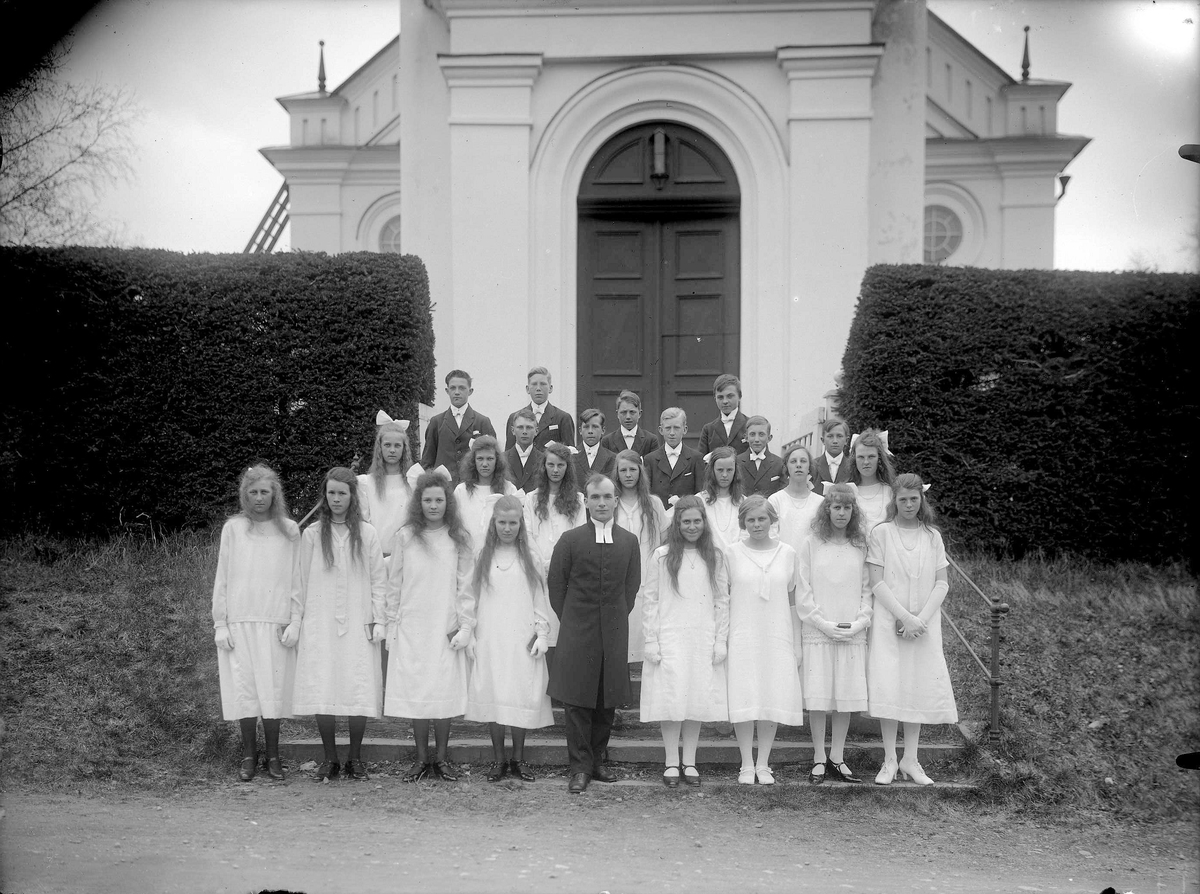Gruppfoto av konfirmander 1926 framför kyrkan med Komminister Berglund.