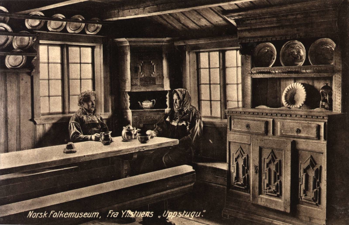 Postkort. Ylistuens "Uppstugu", to kvinner ved langbordet. Telemarkstunet, NF.