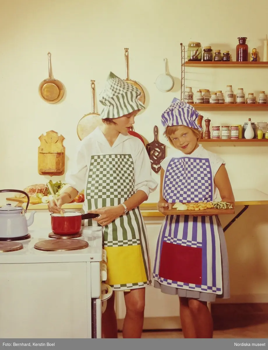 Två flickor med färgglada randiga förkläden i kök