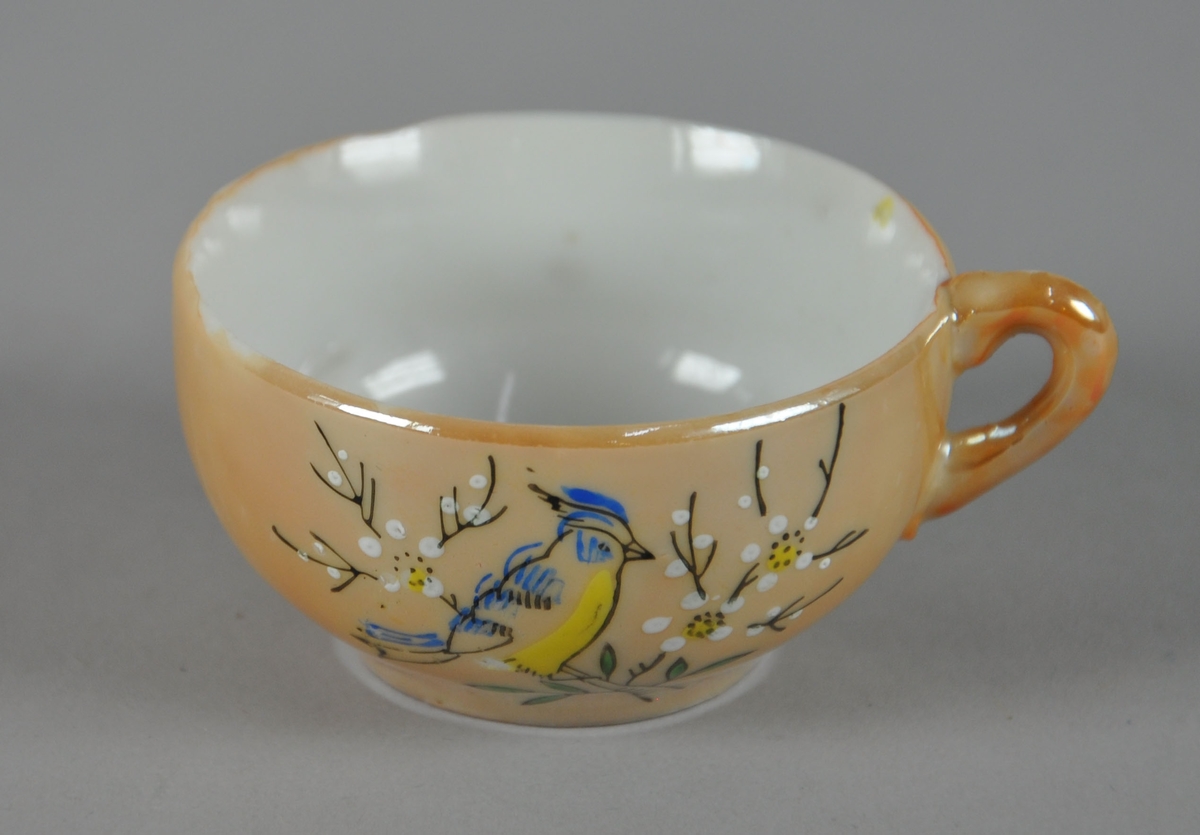 Liten kopp med malt dekor. Koppen har én hank, og utsiden er gullfarget. Malt dekor med motiv av fugl i tre.