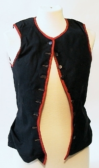 Livstycke för kvinna av svart kläde, kantat med röda ylleband. Livstycket är fodrad med getskinn och knäpps med nio st små mörkgrå knappar.