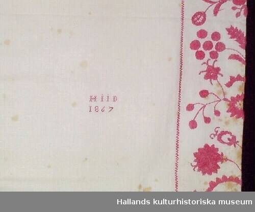 Så kallat putevar av lin. Ena kortsidan är prydd med broderad blomsterbård i ljusrött garn. Märkt: "HIID 1867".