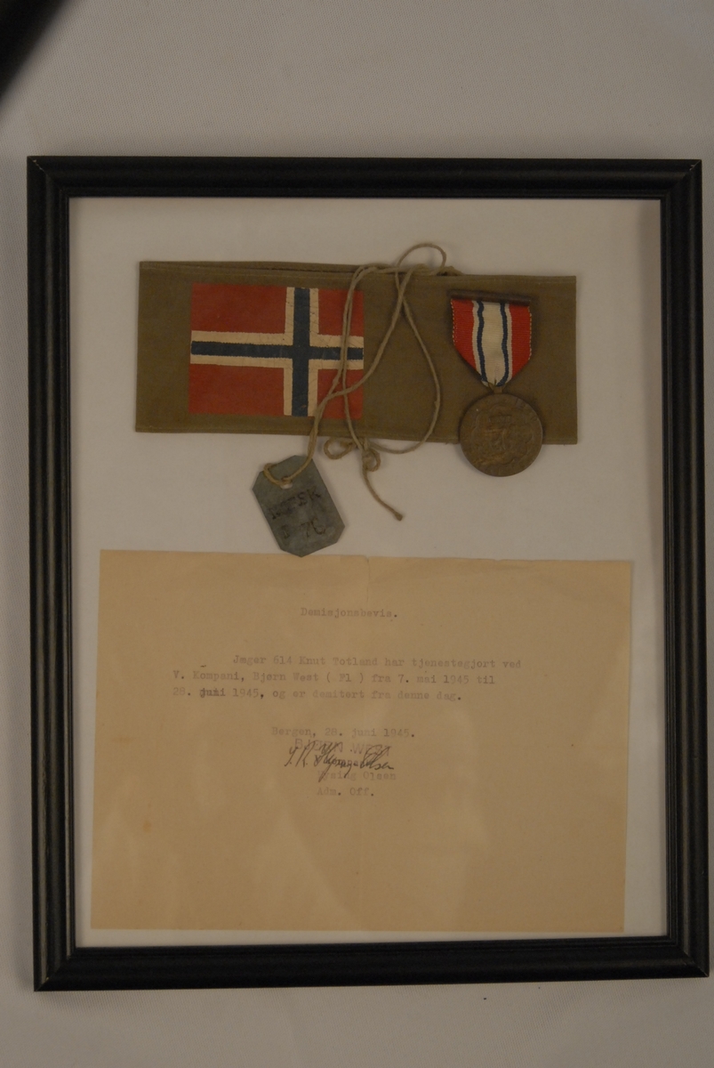 Deltakarmedaljen og eit brunt armbind med det norske flagget påtrykt.