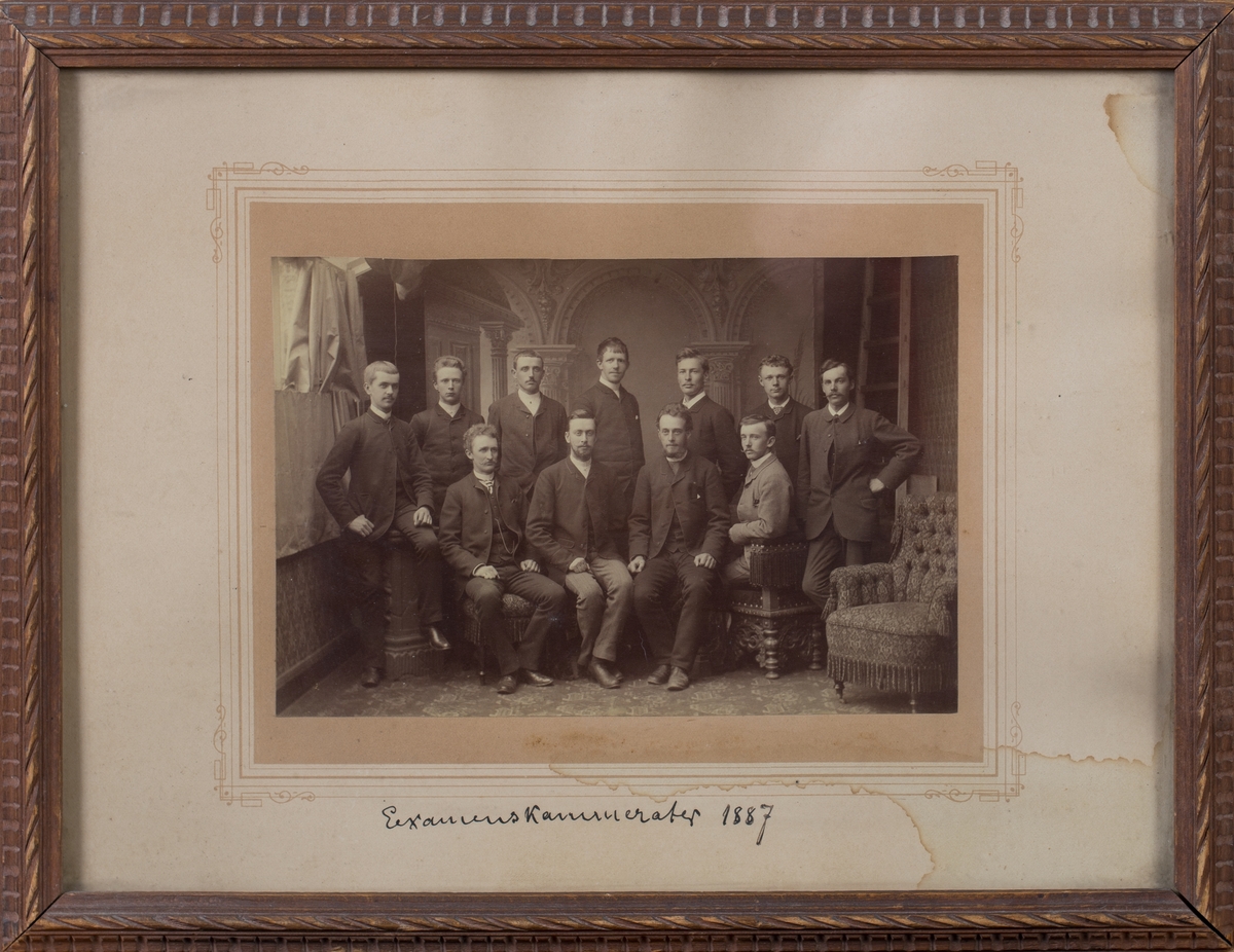 Gruppefoto av fire sittende og sju stående menn. En ørelappstol helt til høyre i bildet.