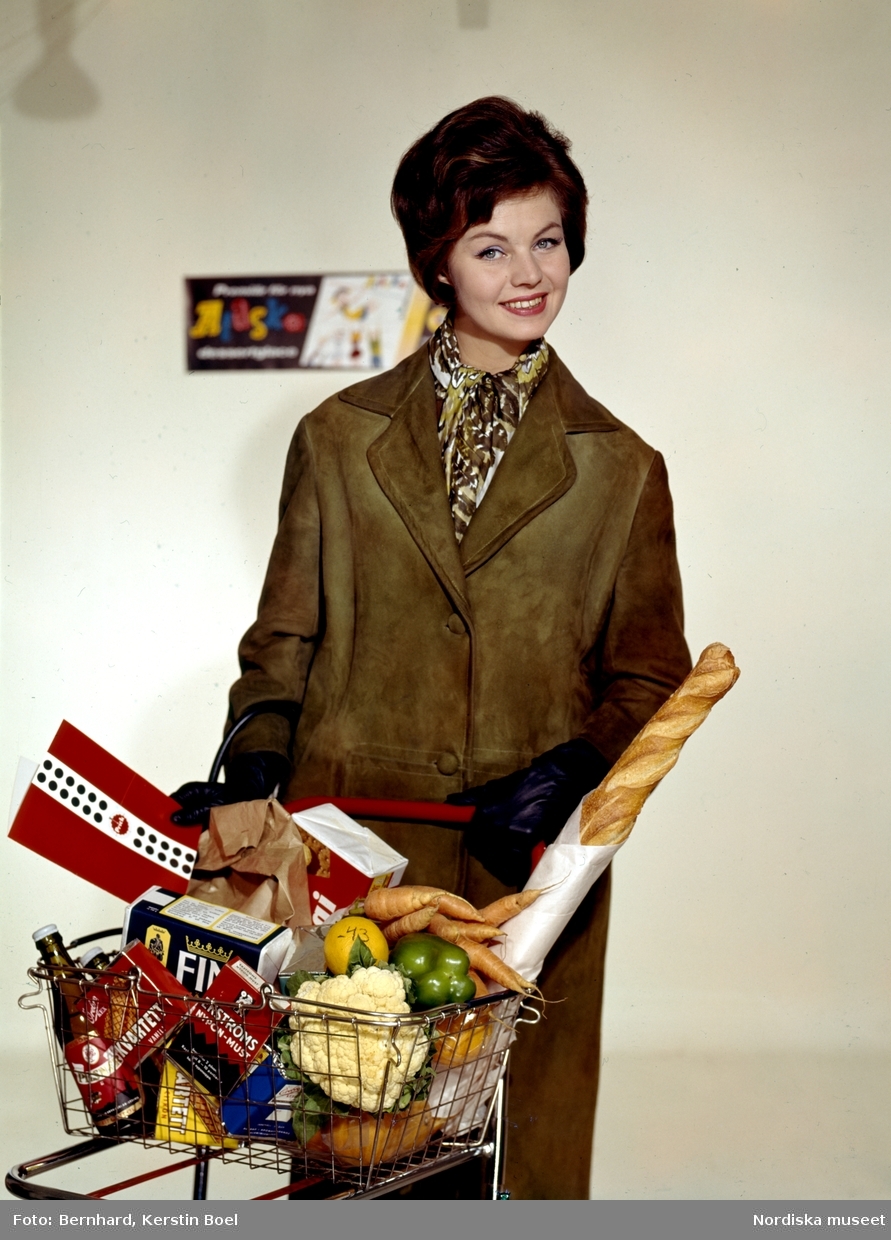 En leende kvinna i brun skinnkappa med kundvagn full av matvaror