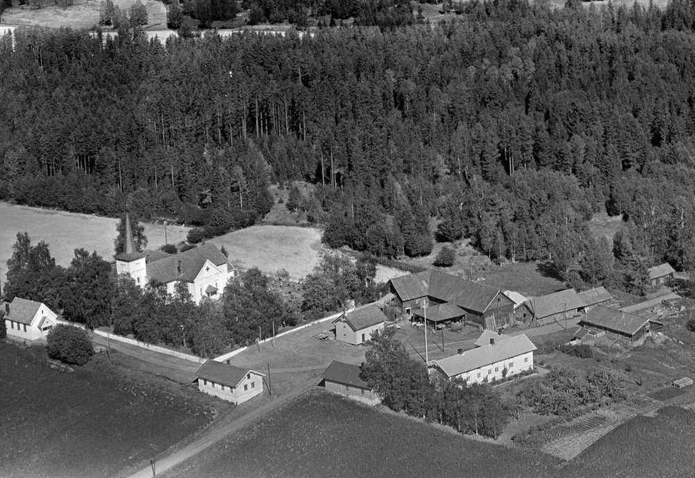 Flyfoto i svart-hvitt som viser Vallset kirke og garden Tomter like ved, før Tomterlåven ble tatt ned og flyttet til museum.