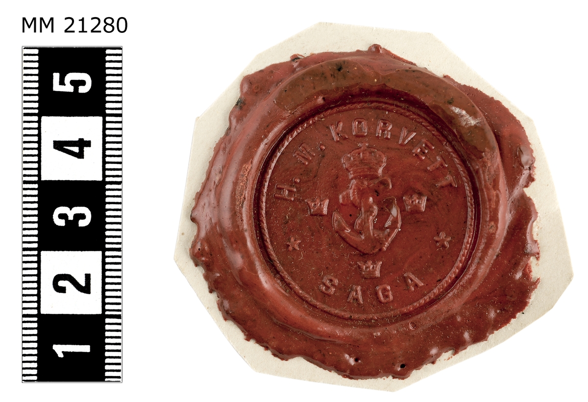 Sigillavtryck av rött lack på papper.
I mitten krönt stockankare omgivet av tre kronor.
Längs kanten text: "H.M. Korvett Saga".