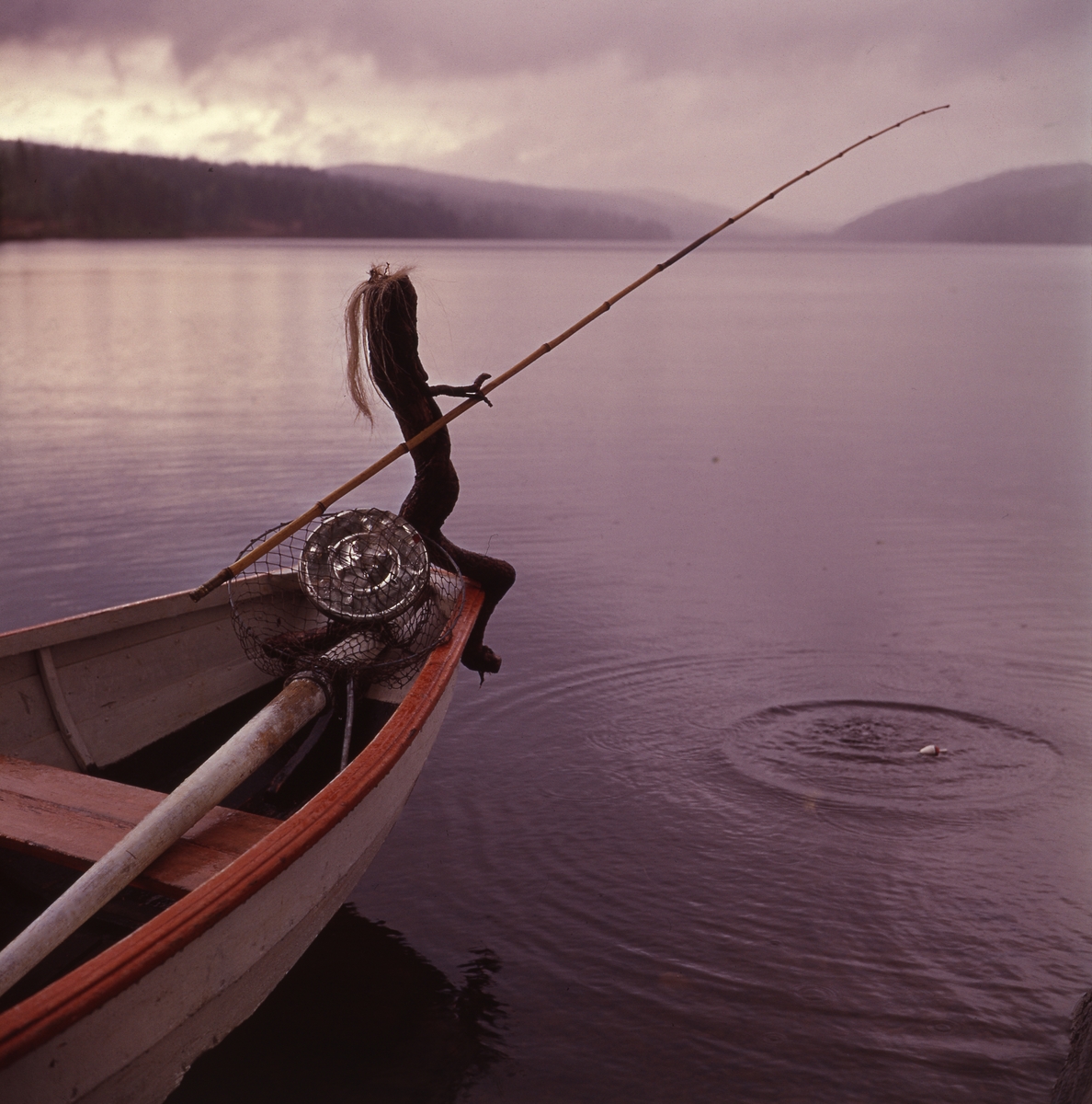 Trätrollet Skrälla Skrälle sitter i fören på en roddbåt på sjön Ängratörn och metar.