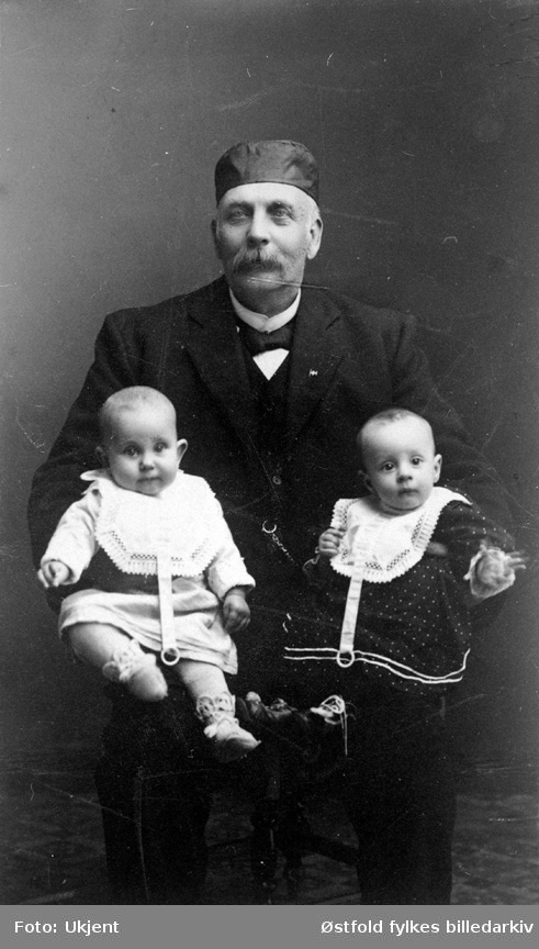 Gruppeportrett av bestefar med barnebarna sine. 
Amund A. Kind, og barnebarn Aase til venstre og Kristin til høyre. 
Rømskog 1911-12.
Amund var poståpner og gårdbruke på gården Trandem.