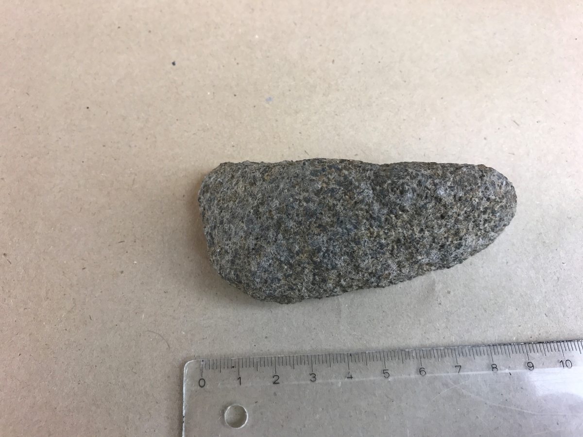 Förarbete till stenyxa?

Stenens form påminner starkt om formen på en lihultyxa, men saknar tydliga tecken på att vara en färdig yxa. Fyndsammanhanget gör ändå att stenen registreras med de övriga fynden från boplatsen.