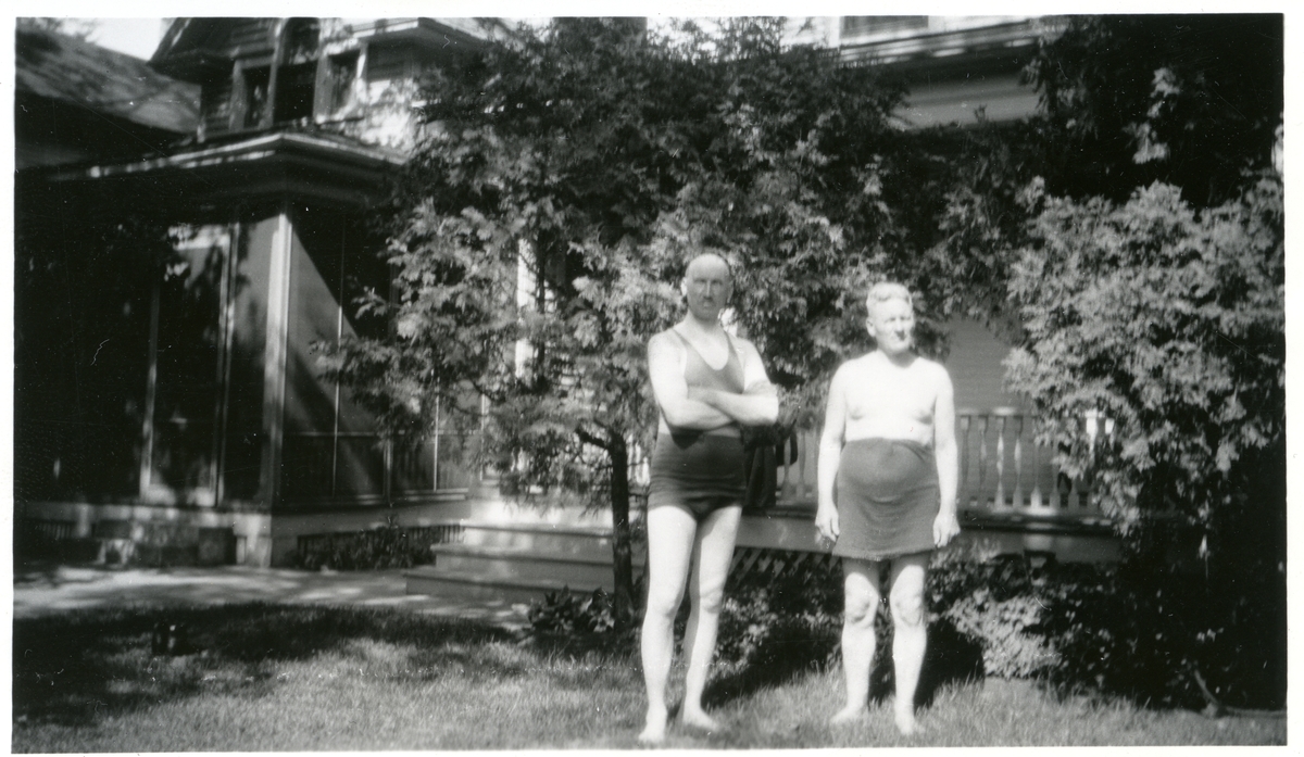 To menn avbildet i badetøy utenfor et hus. Bildet er tatt i Amerika.