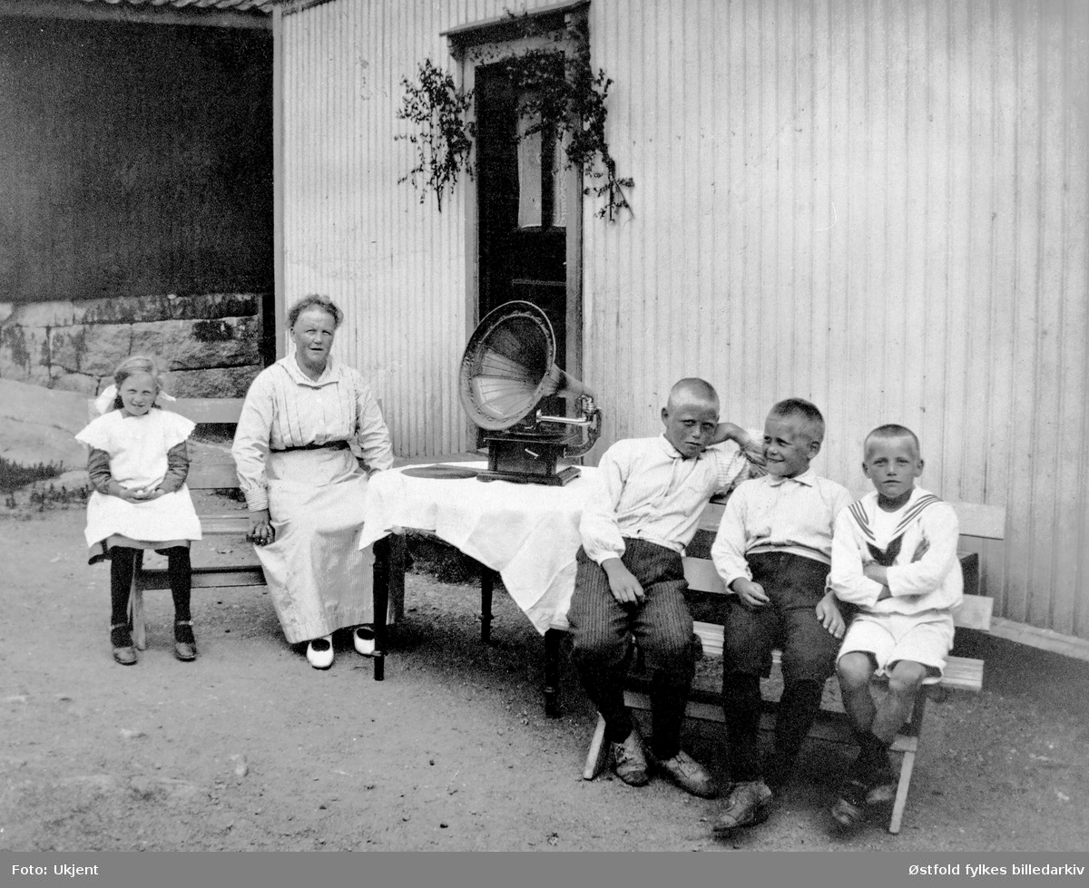 St. Hansfeiring, bruksbebyggelsen, Øyenkilen i Onsøy 1919. 
Tre brødre Kile, deres mor og 11 år gamle Astrid Lilly Hansen sittende utenfor bygning ved bord med tut- grammofon.