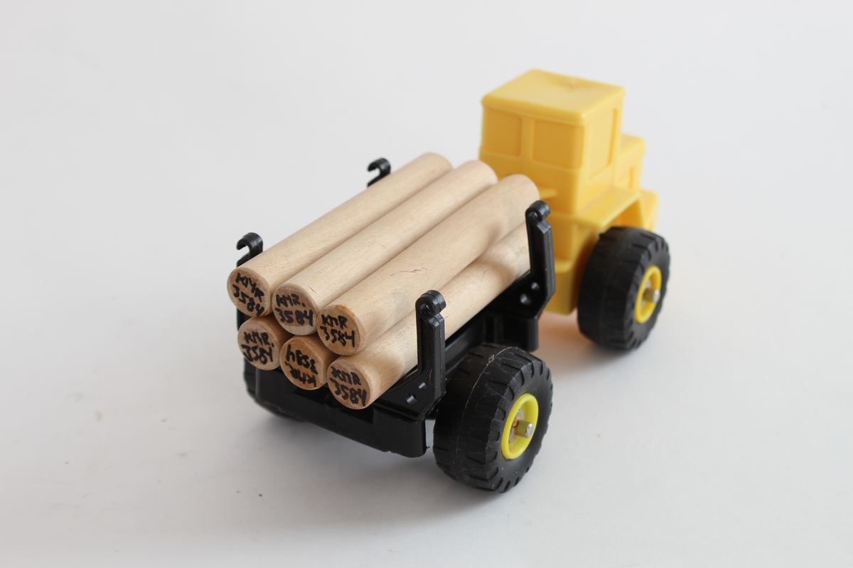 Giver. Bjørn Sverre Hol Haugen (f.1972).
En gul traktor i plastikk, med en svart henger og 6 trepinner som etterligner på tømmer.