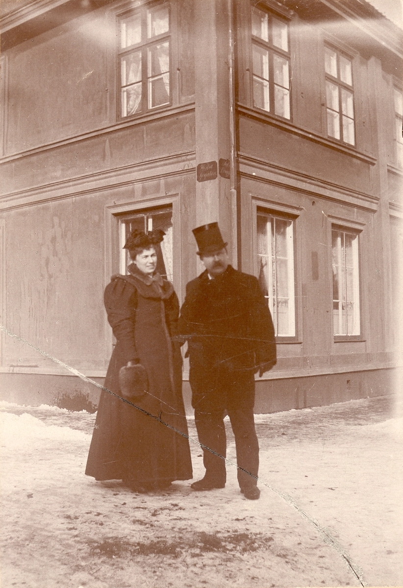 En man i en cylinderhatt och en kvinna står vid hörnet av Västra Sjögatan och Södra Långgatan.