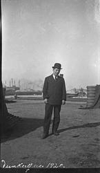 Mann med hatt på kaien i Dunkerque. Havneanlegget i bakgrunn