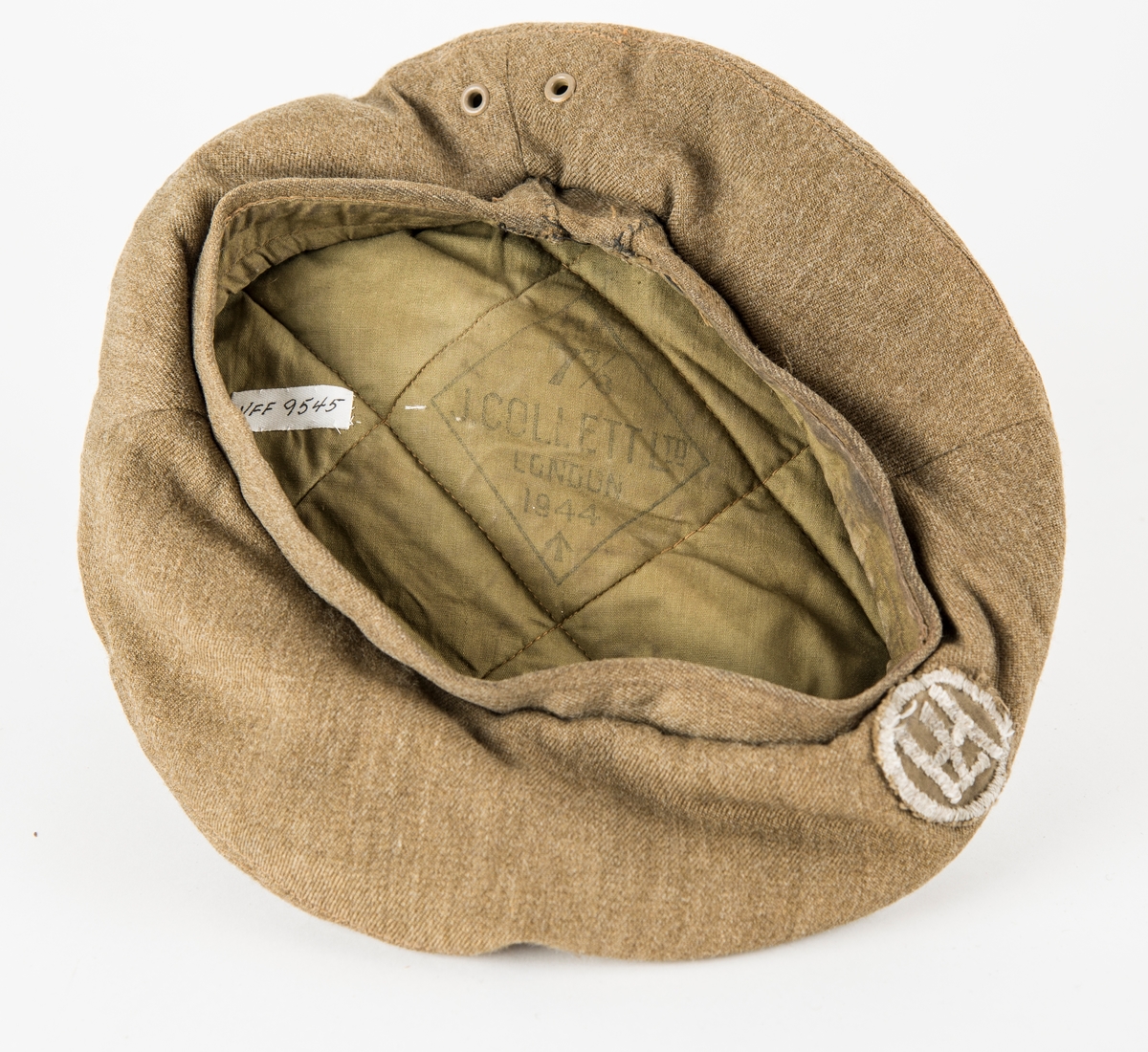 Militærlue, "Beret" i brun-grønt ulltøy. Påsydd merke med Håkon 7. Vattert inni med grønt bomullsstøy og merka med J. Collett Ltd. London 1944