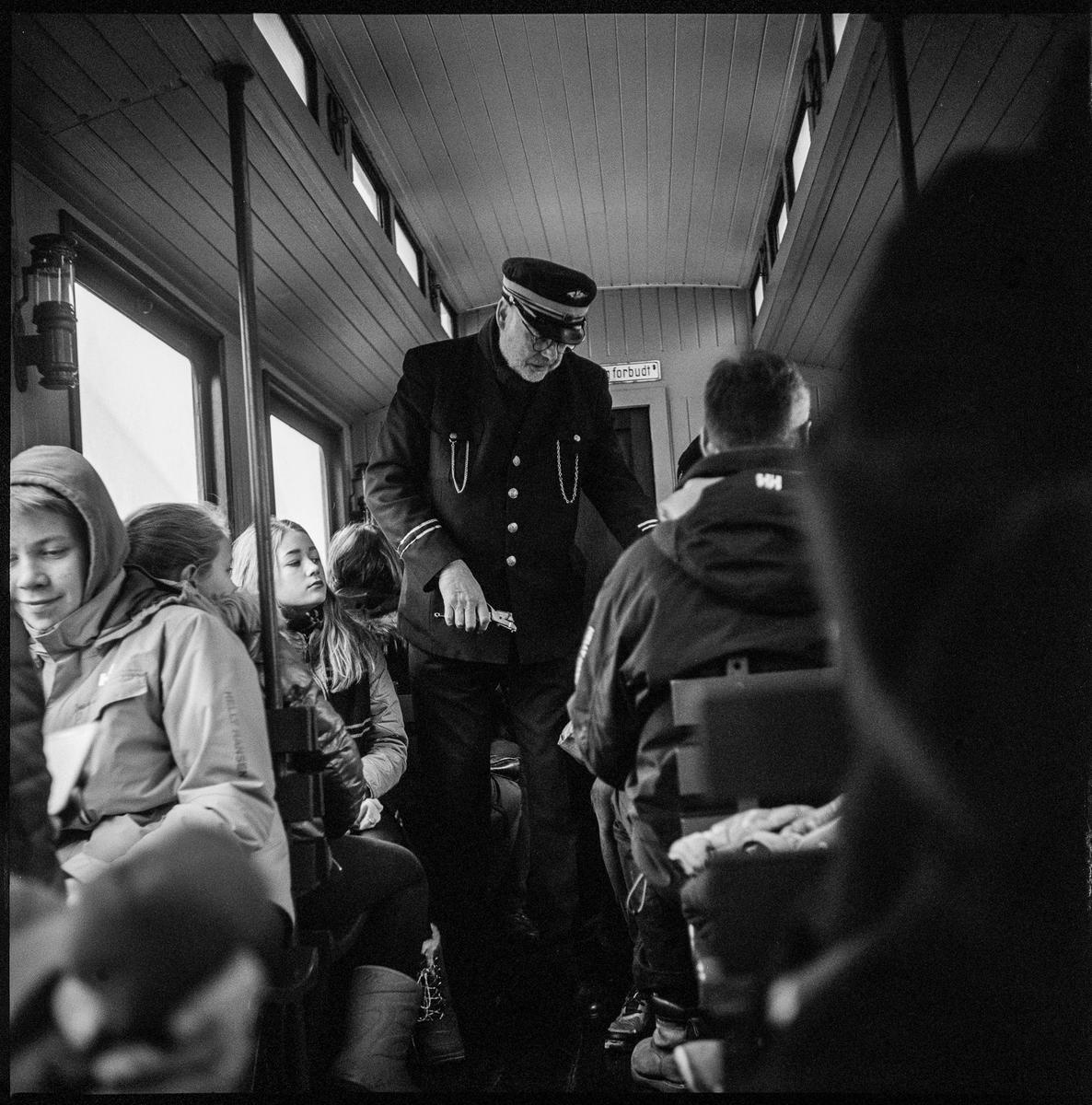 Mannlig uniformert frivillig kontrollerer billettene til reisende i passasjervognen.