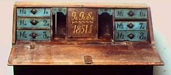 Brunådrad snedklaffbyrå. Klaffen är utvändigt blåmålad med svart växtranka. 6 blåmålade, numrerade lådor samt "JJS 1851" innanför klaffen. Inköpspris 6 kr.