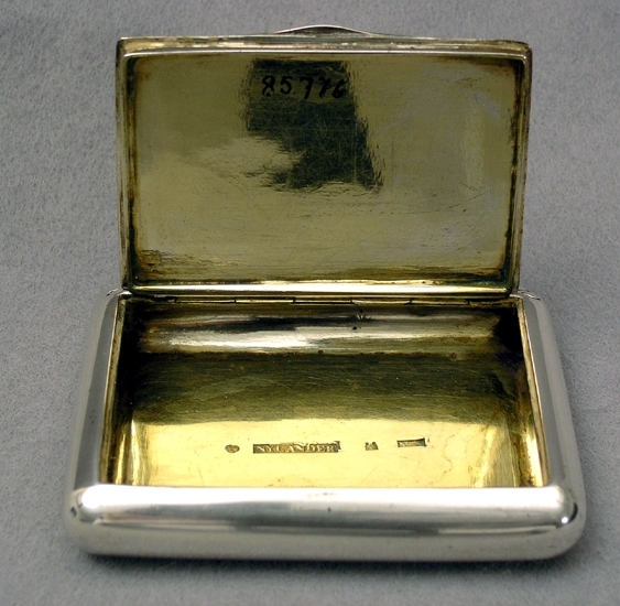 Snusdosa av silver, inuti förgylld. Under botten står: OG 7 1/2 lod. Stämplar: Nylander (Jonas Nylander 1816-) - tre kronor- Skara stadsstämpel-Y3 (1829).