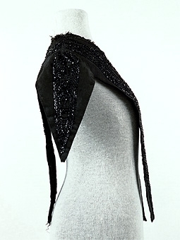 Del av klädningsliv sytt av svart ripsvävt siden, dekorerat med bårder av svarta pärlbroderier. Troligen är pärlorna av glas.
