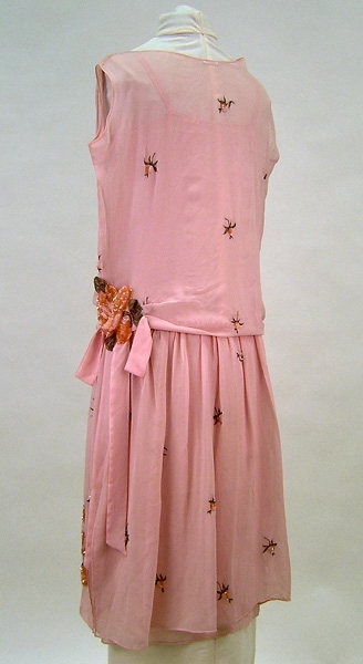 Klänning bestående av kjol med hopsytt linne samt löst hängande blus.
Sydd av tunt, glesvävt kräppat siden. Broderier bestående av glaspärlor, paljetter och metalltråd.