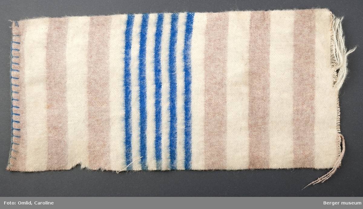 En prøve. Teppe i stripemønster; rosa og hvite striper.  Mønsterbord i smalere striper, fem blå og fire off-white.