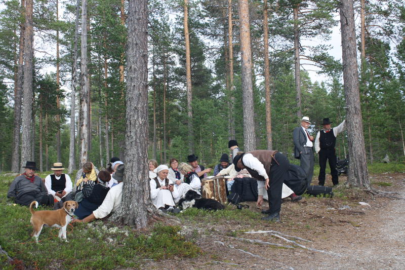En gruppe mennesker i tradisjonelle klær sitter i skogkanten.