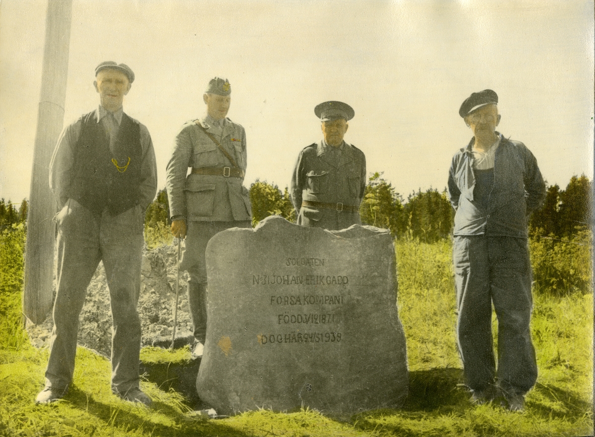 Grupporträtt av fyra män vid minnessten över soldat från Hälsinge regemente I 14.