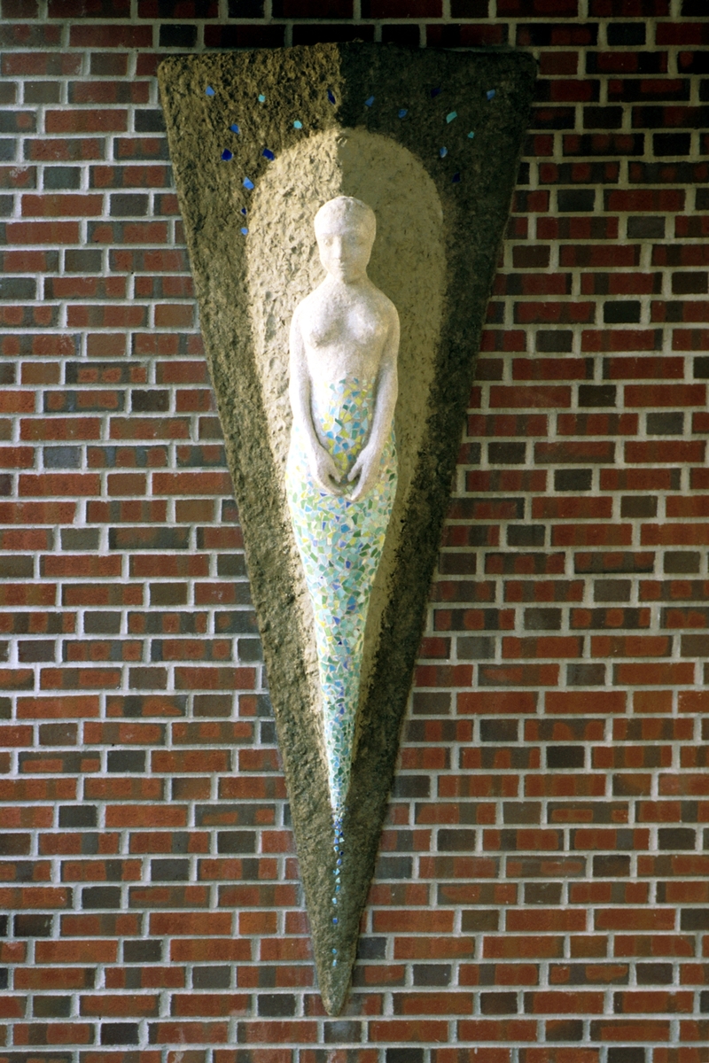 Utsmykkingen består av en figurativ veggskulptur utformet som en kvinneskikkelse/gallionsfigur. Figuren fremtrer på en bakgrunnsform, et relieff som gir assosiasjoner til baugen på et skip.