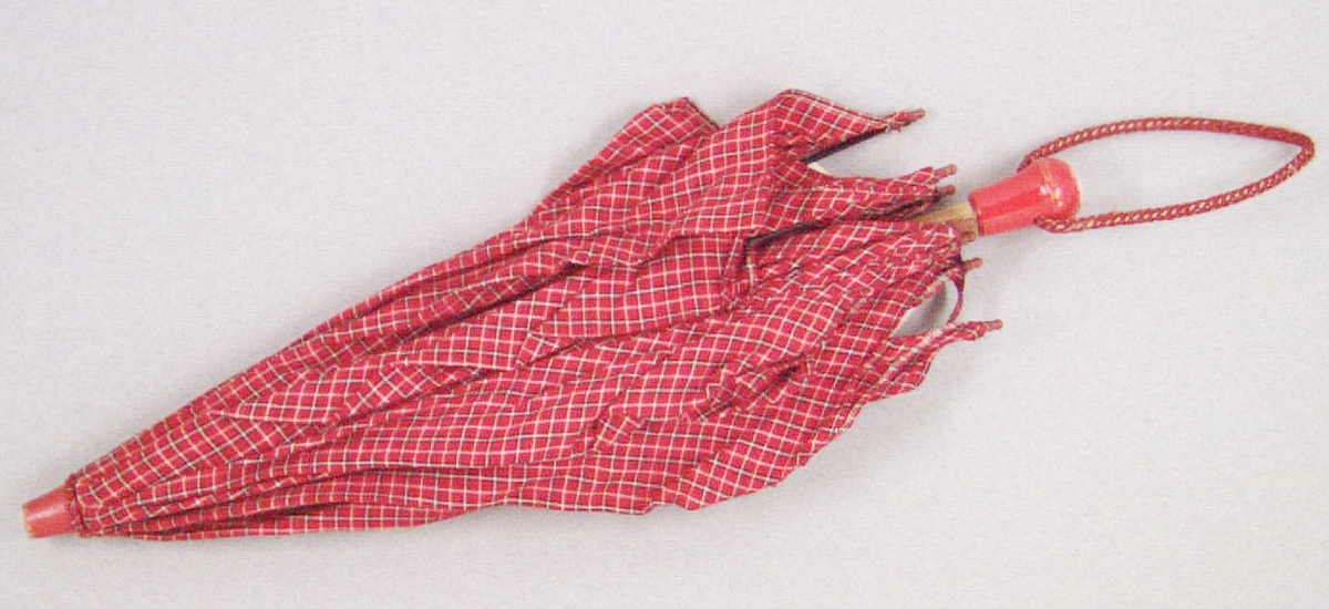 Ett leksaksparaply av rödrutigt bomullstyg på trästativ. Spröt av metall. Längst upp och ned rödmålade kulor, försedd med armledssnodd av rött rep.
Har tillhört och använts av Maria Hellquist (född 1943 ) i slutet av 1940-talet.