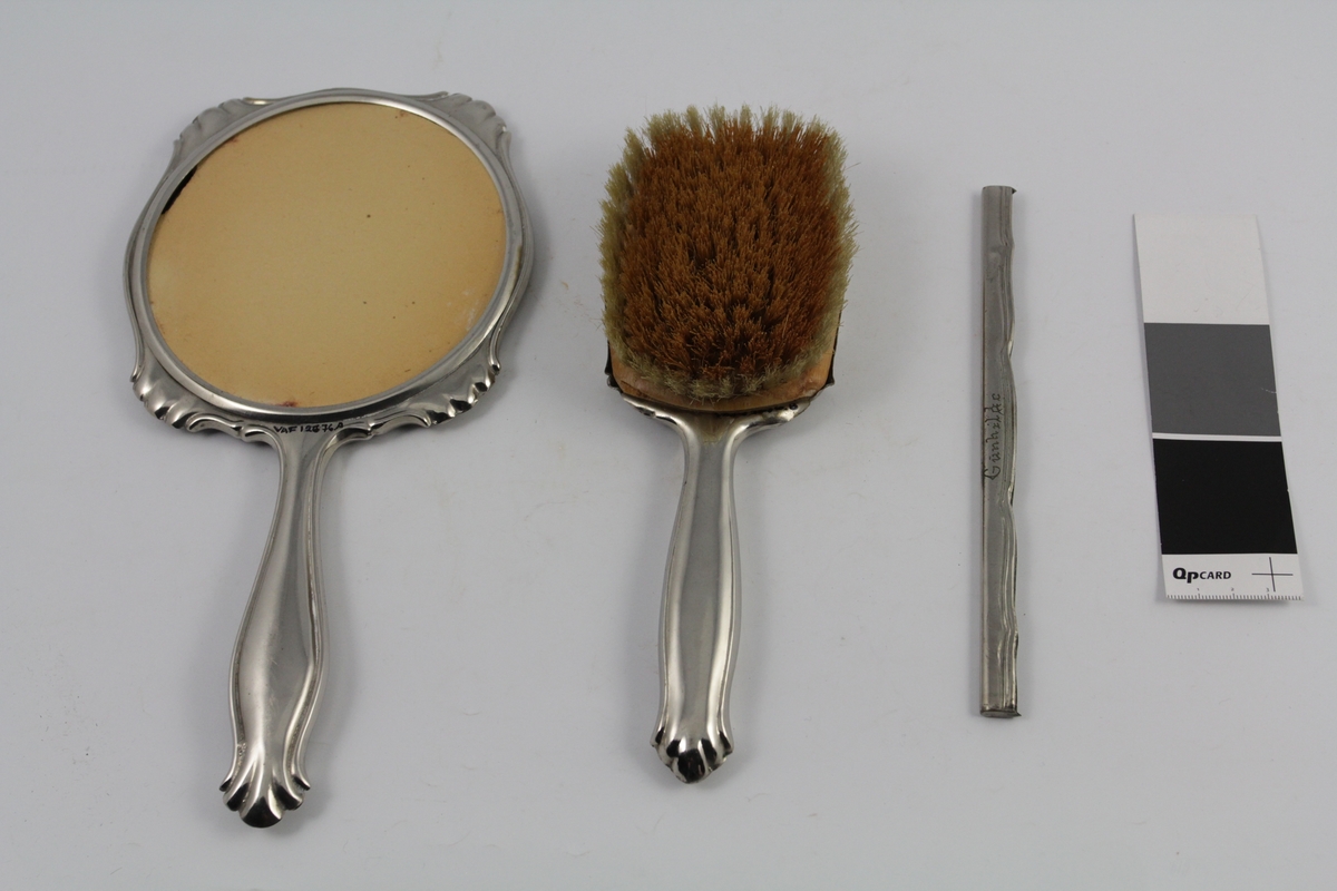 Sett med speil, børste og ramme til kam. Formet og rundet. Speil og hårbørste med håndtak. Gravert tekst.