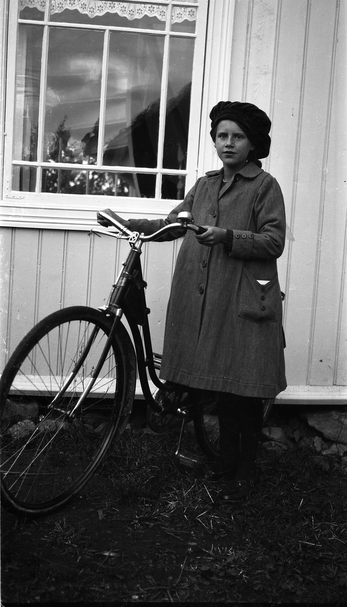 Uidentifisert ung jente med sykkel ved en husvegg.