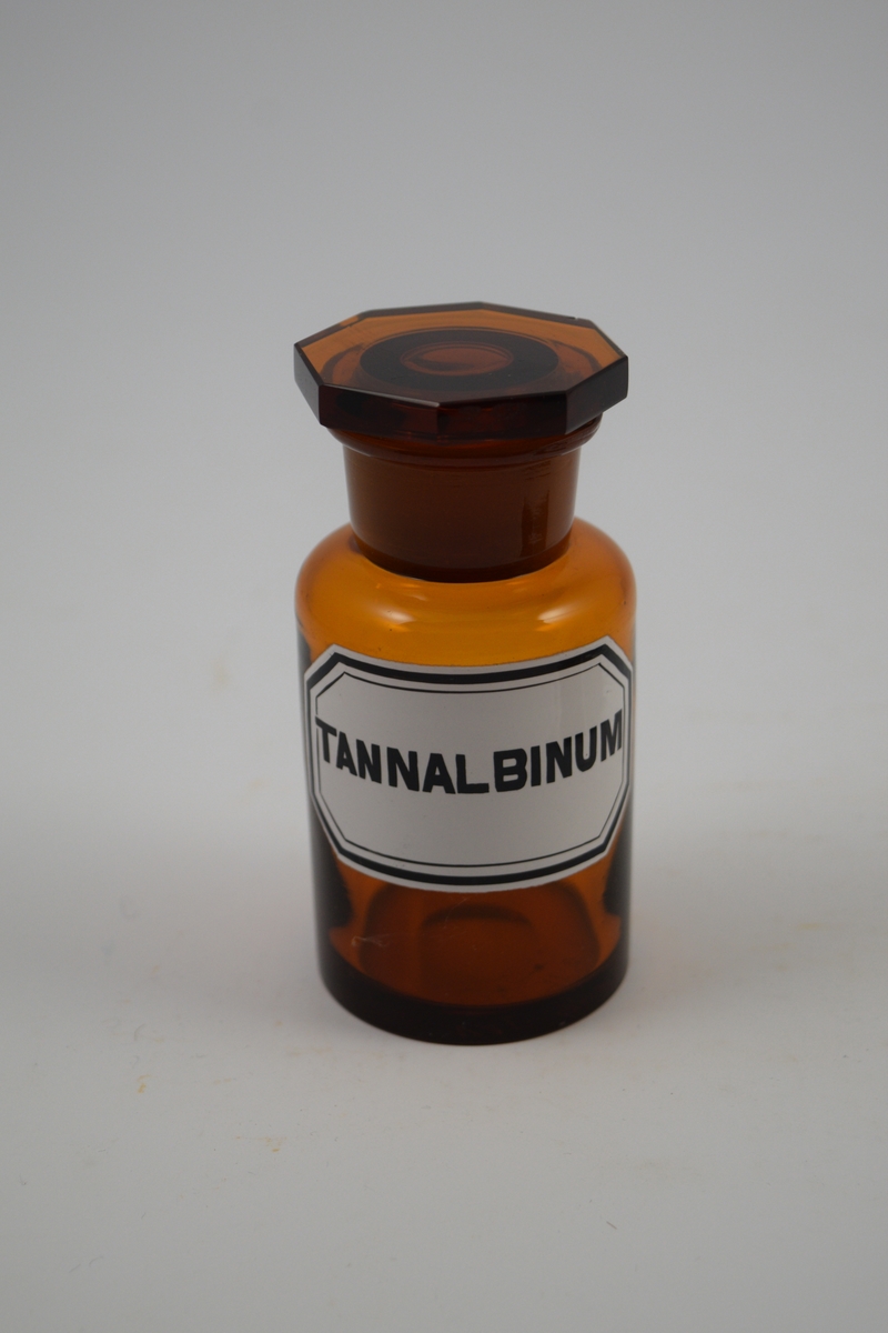 Brun glasskrukke med glasspropp. Hvit etikett med sort skrift. Har inneholdt Tannalbin, brukes mot diare.