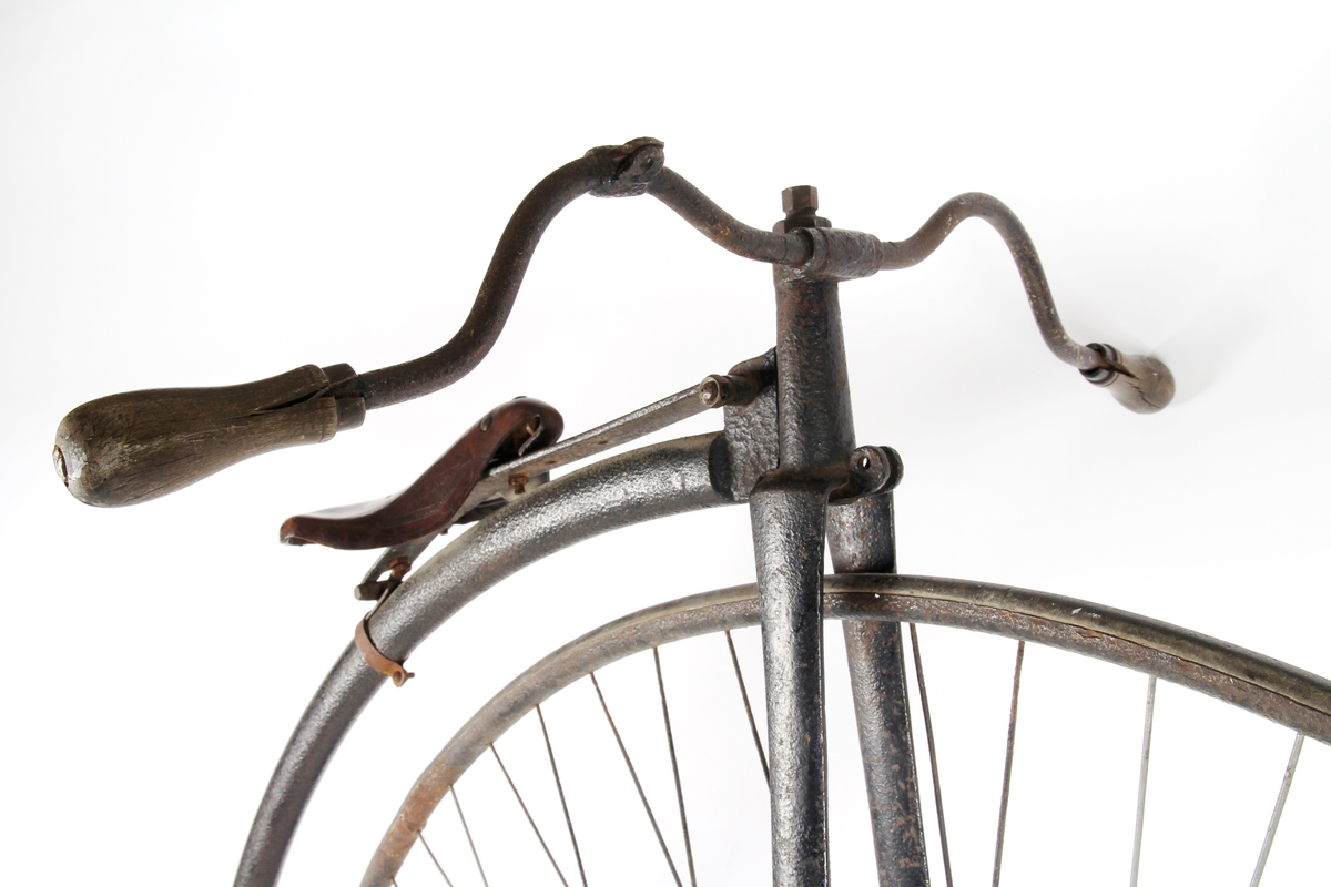 Sortlakkert velosiped med stort forhjul og lite bakhjul. Pedalene er montert direkte på fornavet og setet er plassert rett over.