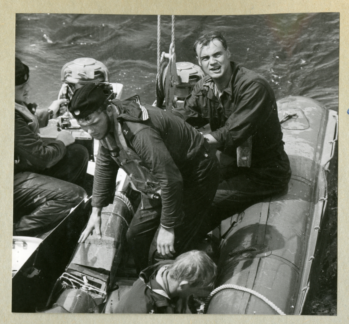Bilden föreställer fyra män i småbåtar under minfartyget Älvsnabbens långresa 1966-1967.