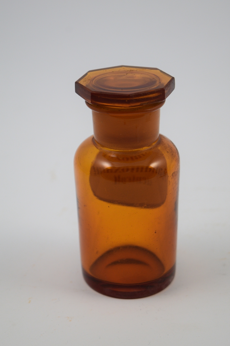Brun glasskrukke med glasspropp. Etikett hvit med sort skrift. Kaliumoxalat - til bruk i legemiddelproduksjon.