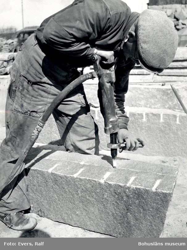 En man borrar i ett granitblock för att klyva det, i fickan har han en tumstock