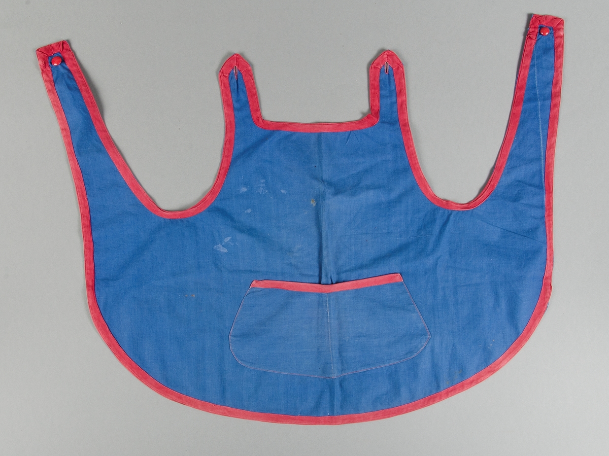 Förkläde för barn av blå bomullslärft kantat med röda band, sytt i ett stycke med rundad nederkant, bröstlapp och axelband som knäpps med röd knapp på axlarna. Bred ficka på magen.