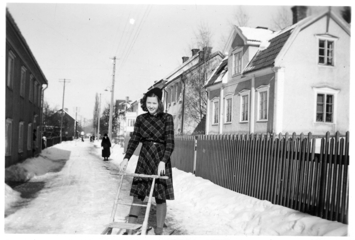 Maj-Britt Axelsson i rutig kappa med sparkstötting på Bergsgatan utanför nr 42