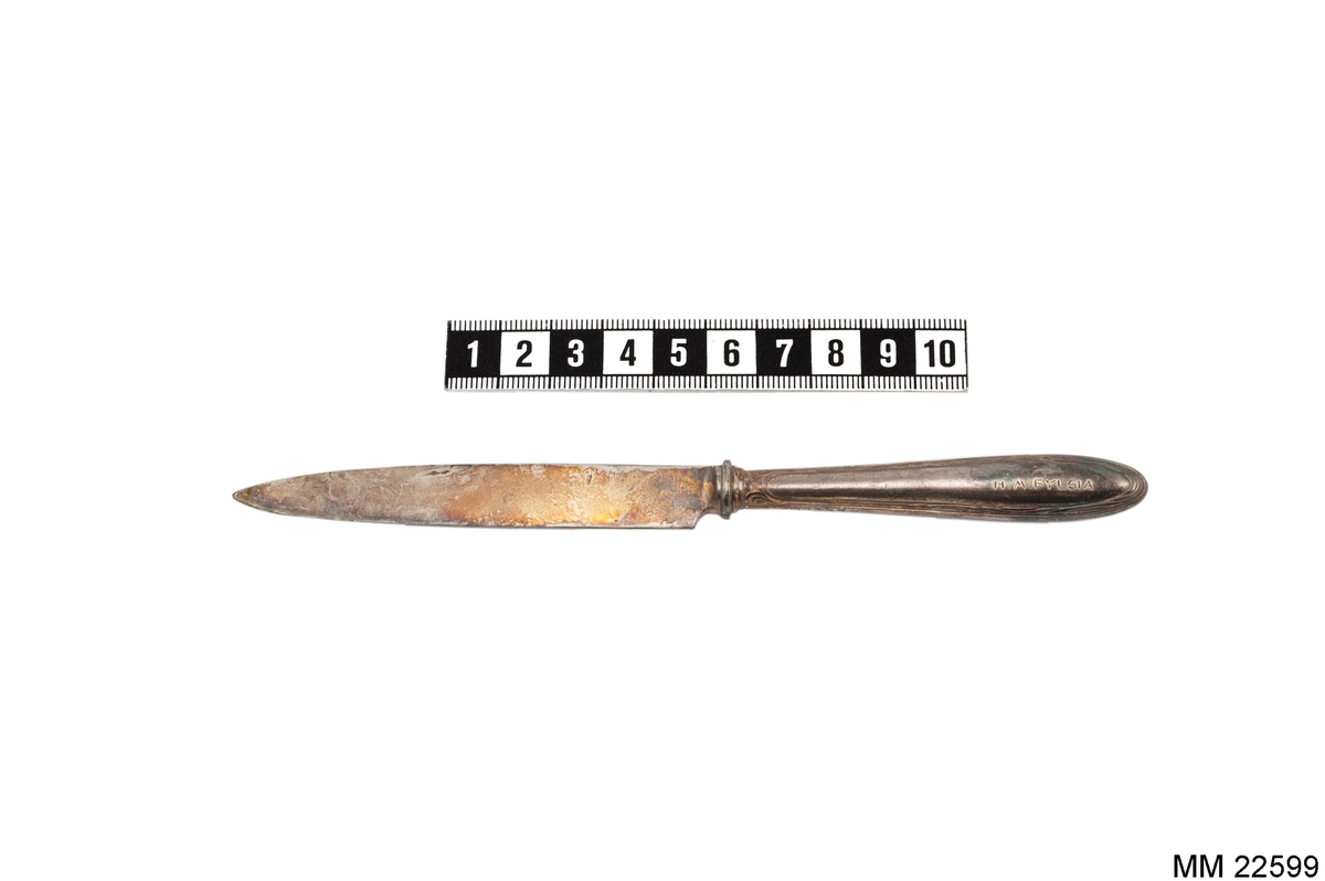 Fruktkniv, skaft med vågformad slinga längs kanten.
Märkt på skaftet: "H.M. FYLGIA" samt på knivbladet: "KA ALPACCA 45GR".