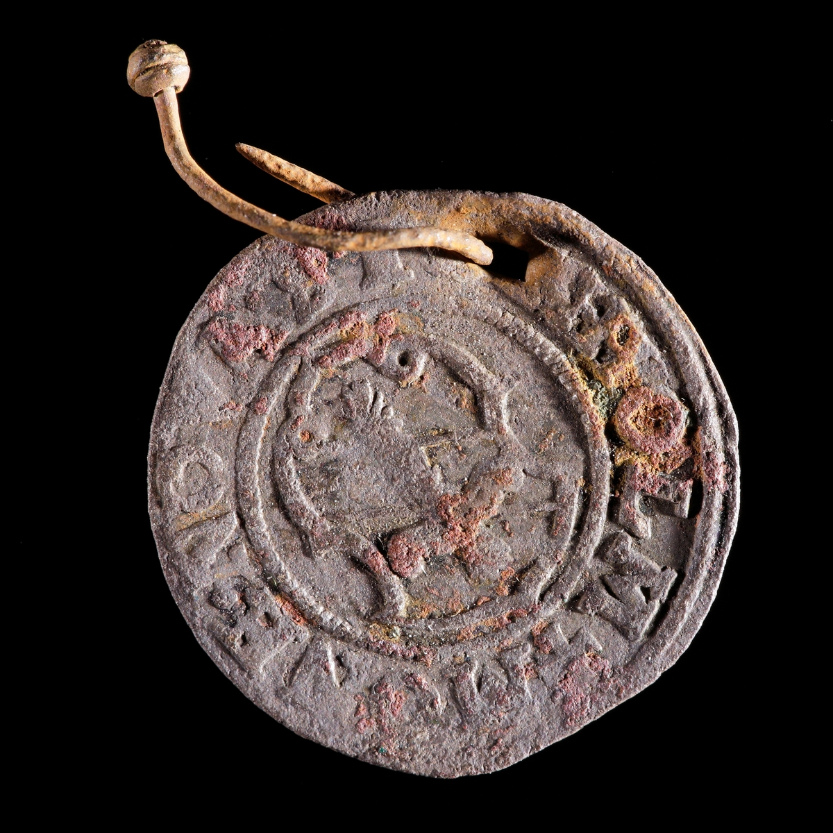 Mynt. 1/2 öre myntat av Erik XIV 1565. Hål med vidsittande knappnål av järn. Åtsida med krönt E och frånsida med Vasavapnet.