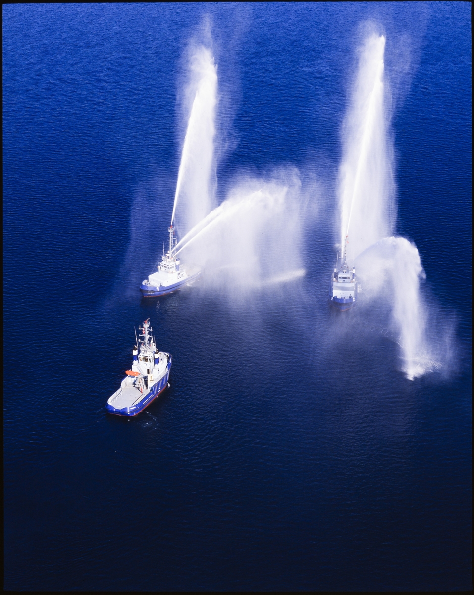 To av tre taubåter spruter vann i ulike retninger på sjøen.