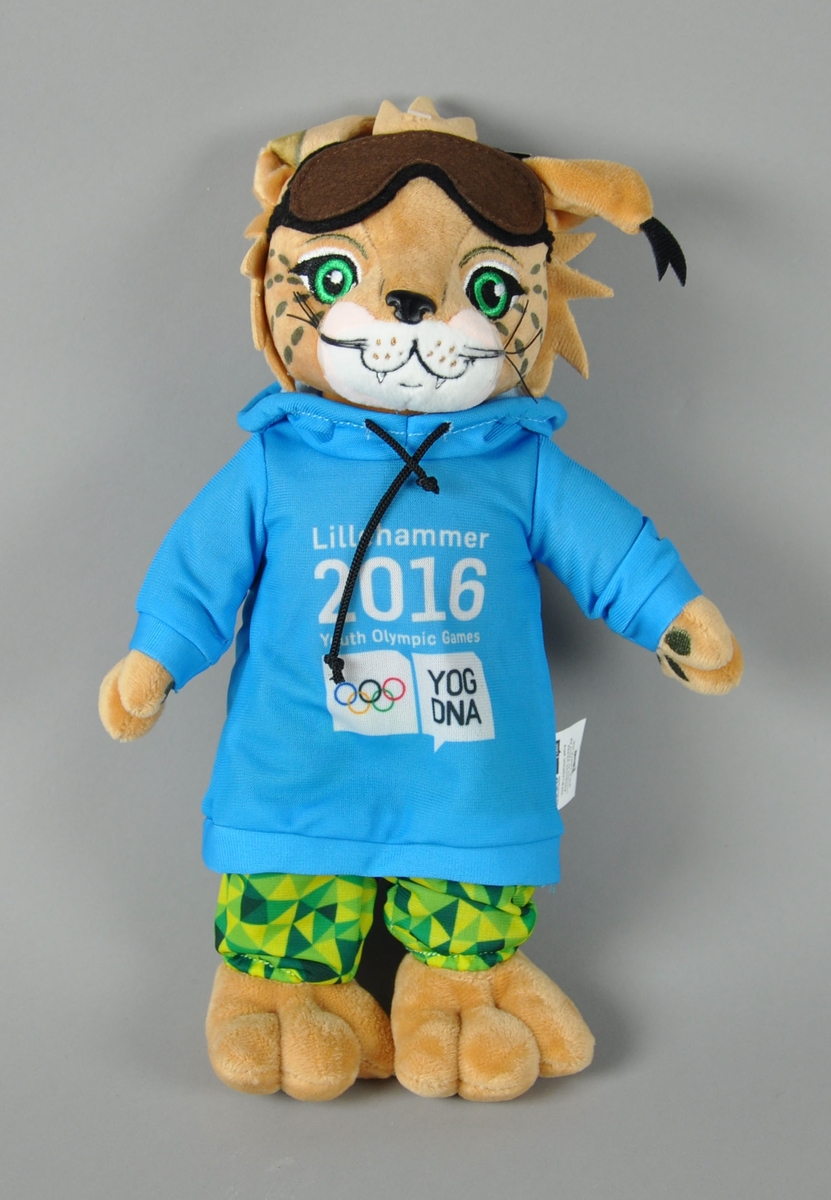 Maskot - en gaupe kalt Sjogg - ikledd lyseblå hettegenser, grønne bukser og brune slalombriller. Genseren har logo for Lillehammer 2016 Youth Olympic Games.