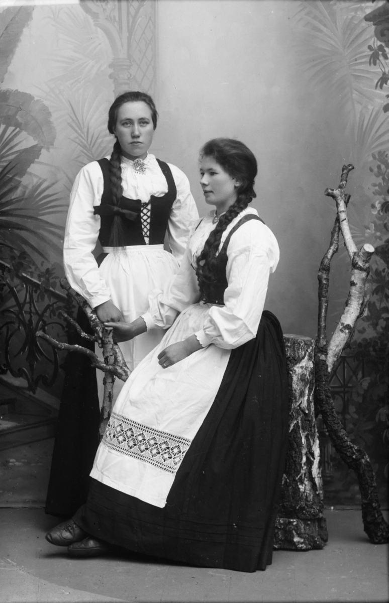 To kvinner i nasjonaldrakt, hvor Marit Røine sitter på en stol og Berthe Marie Skjervum står ved siden av.
