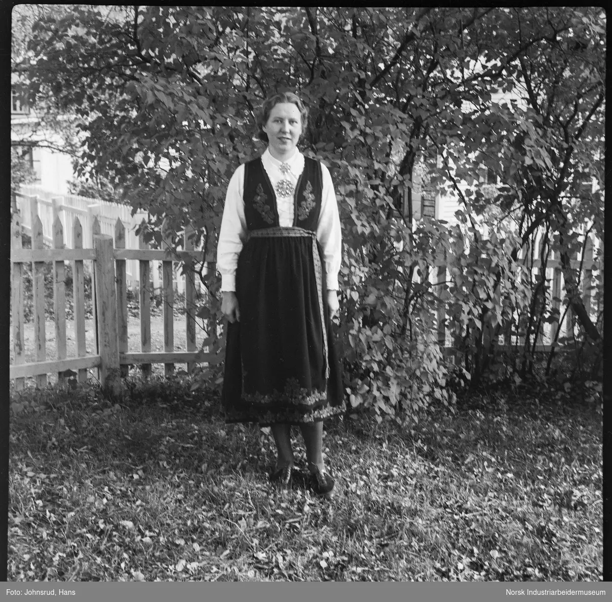 Portrett, kvinne stående i hage kledd i bunad. Elev ved Husmorskolen.