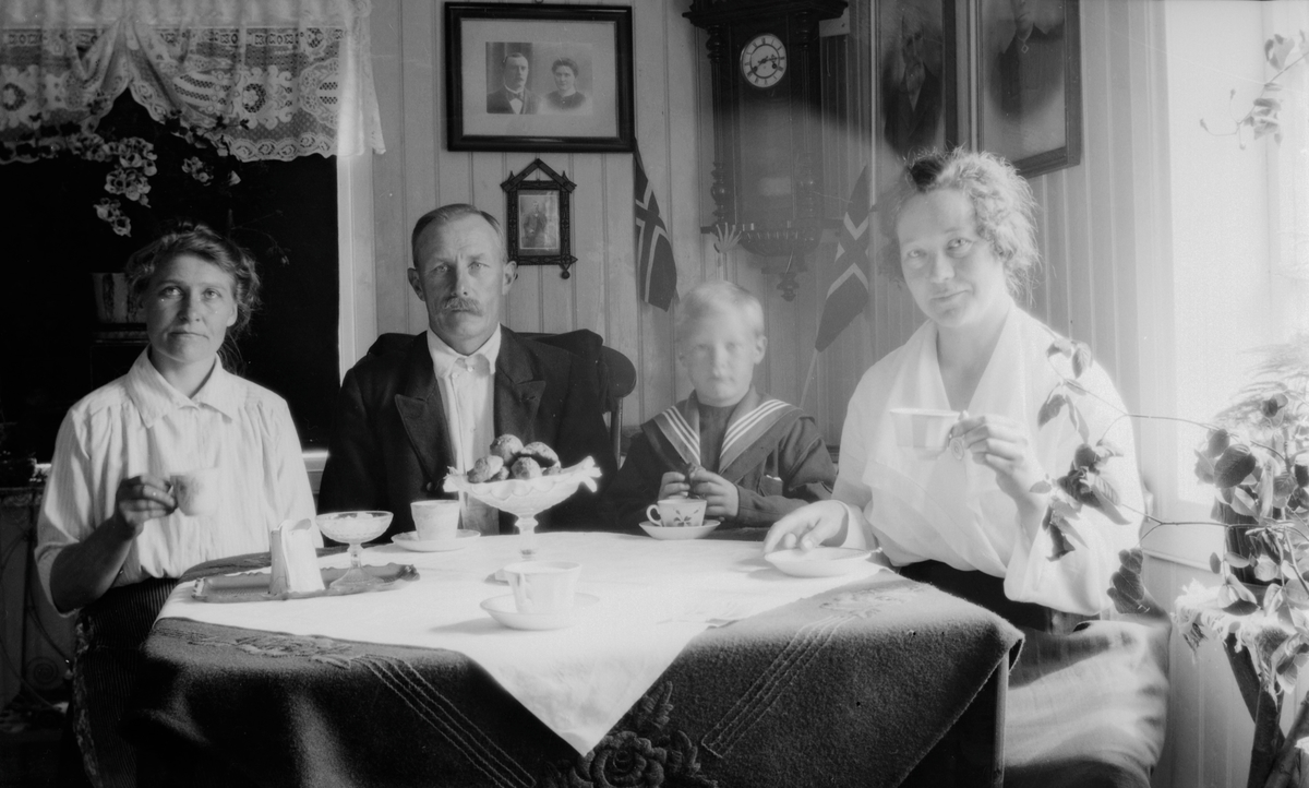 To kvinner, mann og gutt sitter til bords med te/kaffe.